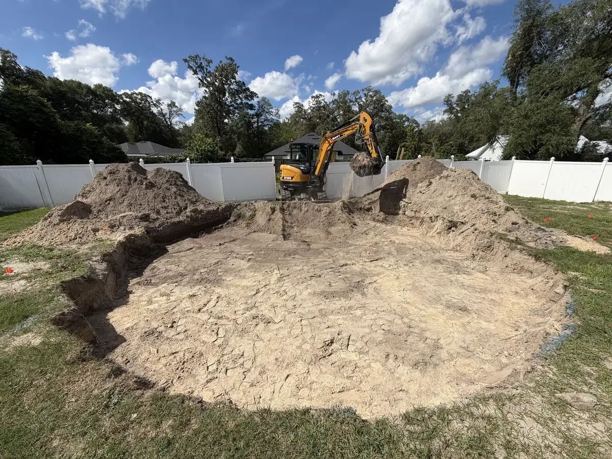 Excavator moving soil within a marked backyard excavation.