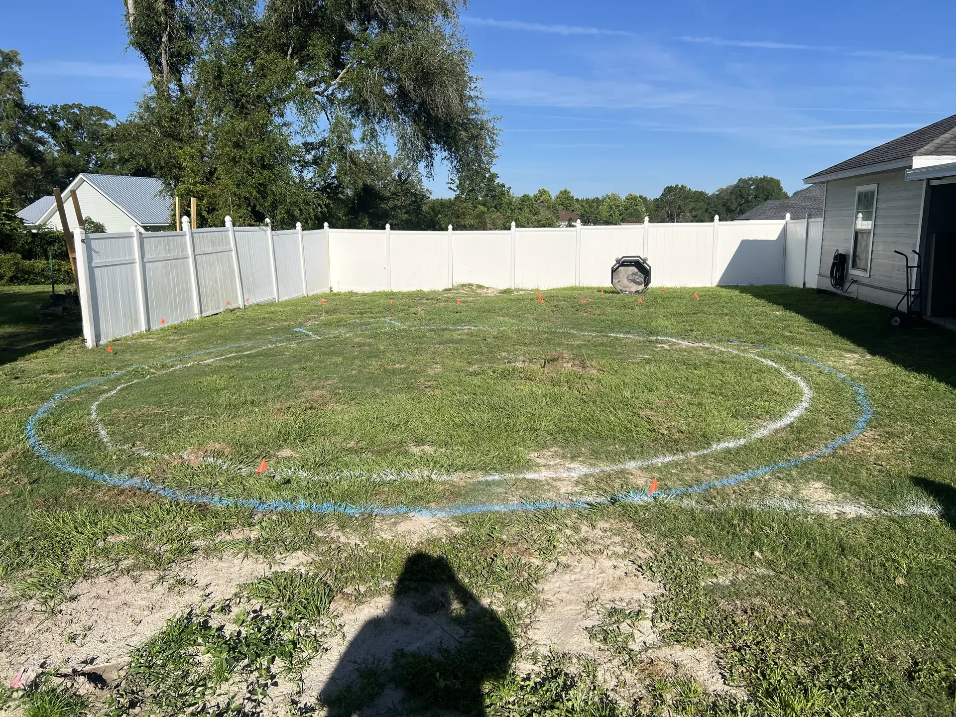 Circular excavation layout marked on grass inside a fenced yard.