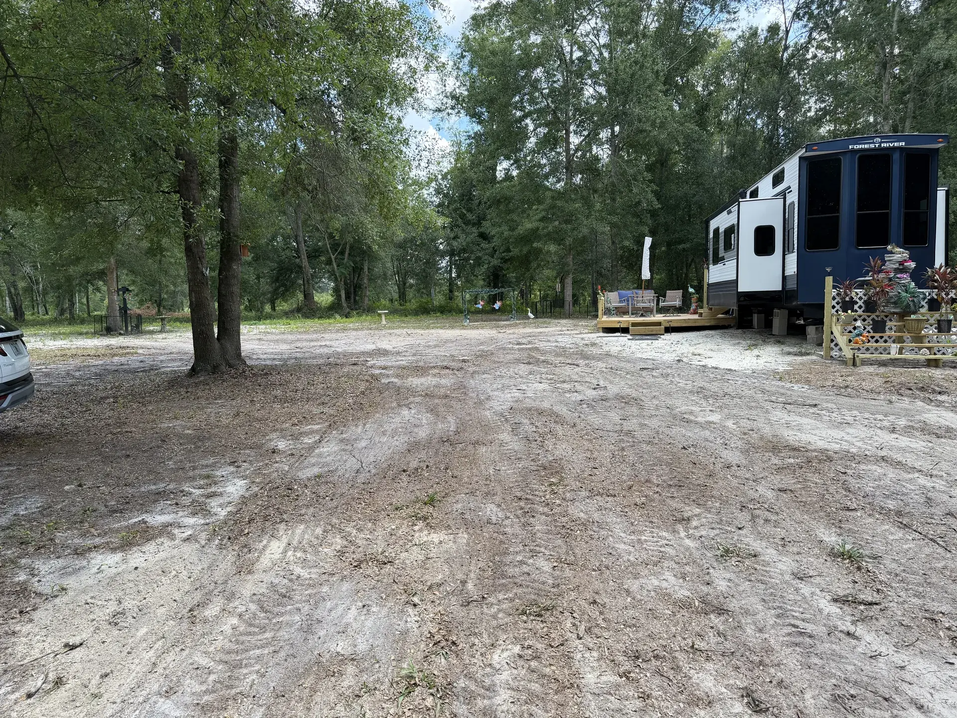 Worked sandy ground around retained trees beside a travel trailer.